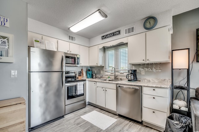 kitchen with white cabinetry, a textured ceiling, light wood-type flooring, sink, and stainless steel appliances