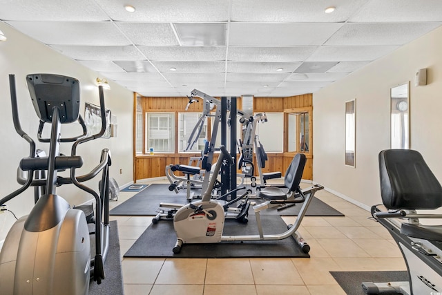 exercise room with a drop ceiling, light tile patterned floors, and wooden walls