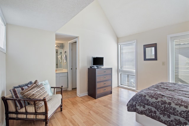 bedroom with a textured ceiling, light hardwood / wood-style floors, lofted ceiling, and ensuite bathroom