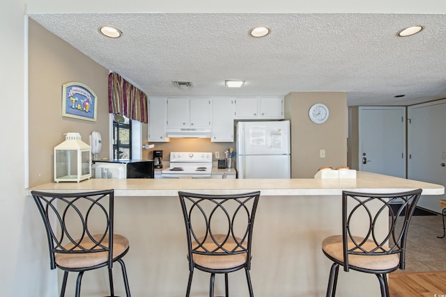 kitchen featuring light wood-type flooring, a kitchen bar, white appliances, and white cabinetry