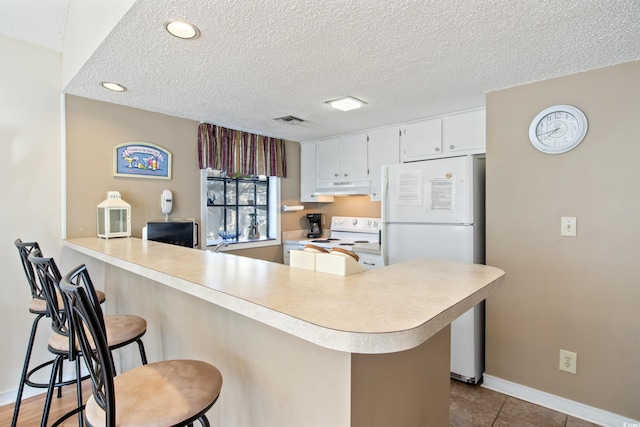 kitchen featuring a kitchen bar, kitchen peninsula, white cabinets, and white appliances