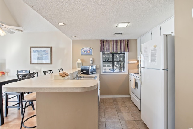 kitchen featuring ceiling fan, kitchen peninsula, white appliances, a breakfast bar area, and white cabinets