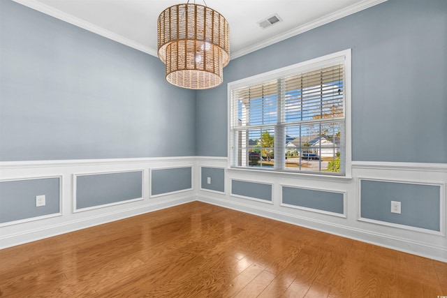 empty room with a notable chandelier, hardwood / wood-style flooring, and crown molding