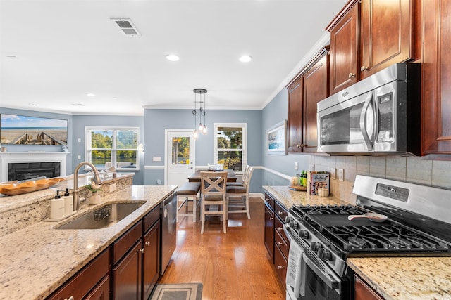 kitchen featuring appliances with stainless steel finishes, ornamental molding, sink, light hardwood / wood-style floors, and decorative light fixtures