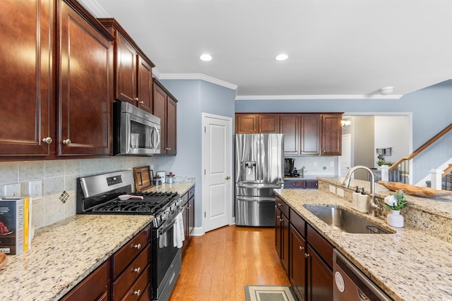 kitchen with light stone counters, appliances with stainless steel finishes, light hardwood / wood-style flooring, ornamental molding, and sink