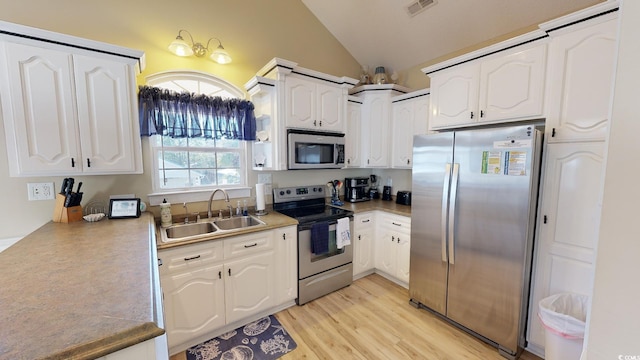 kitchen featuring white cabinets, appliances with stainless steel finishes, vaulted ceiling, and sink