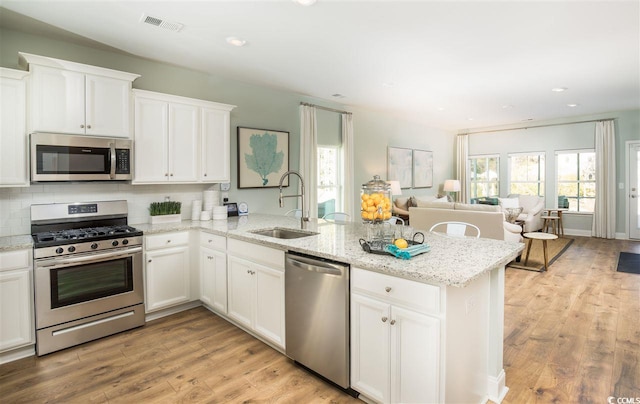 kitchen with sink, kitchen peninsula, white cabinetry, stainless steel appliances, and light hardwood / wood-style flooring