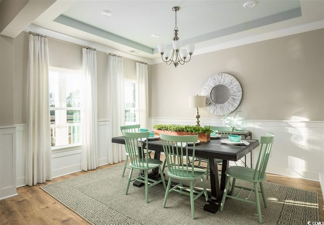 dining space with a notable chandelier, a raised ceiling, and wood-type flooring