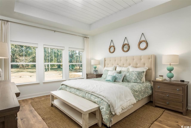 bedroom with a tray ceiling, light wood-type flooring, and wooden ceiling