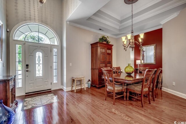 dining area featuring a raised ceiling, crown molding, a chandelier, and light hardwood / wood-style flooring