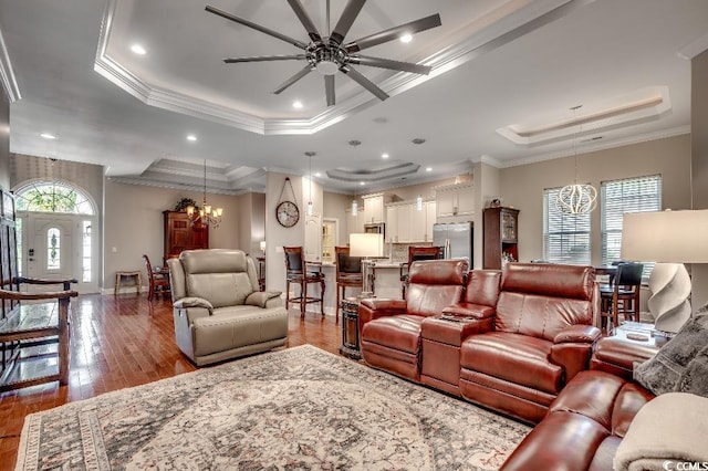 living room with ceiling fan with notable chandelier, ornamental molding, light hardwood / wood-style floors, and a tray ceiling