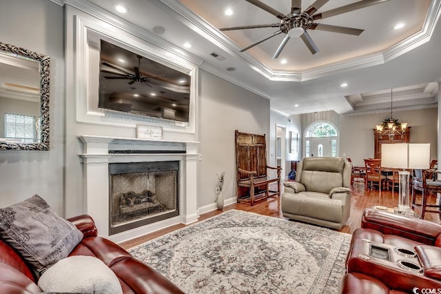 living area featuring wood finished floors, visible vents, a fireplace, ornamental molding, and ceiling fan with notable chandelier