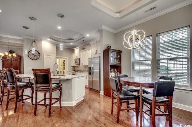 kitchen with decorative light fixtures, sink, a tray ceiling, ornamental molding, and stainless steel appliances