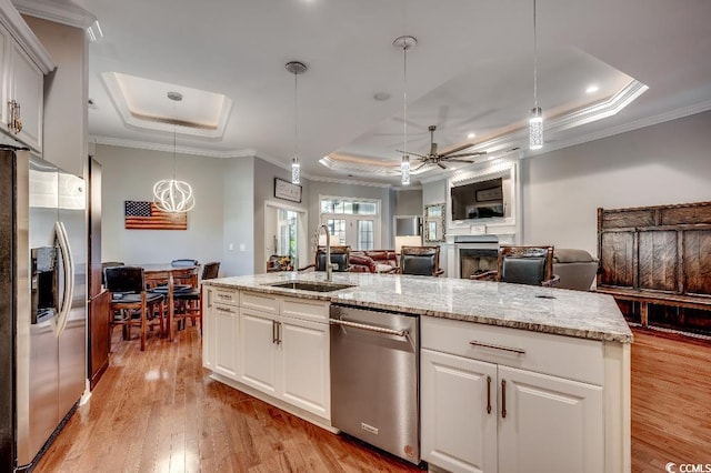 kitchen featuring a sink, a tray ceiling, open floor plan, appliances with stainless steel finishes, and light wood finished floors