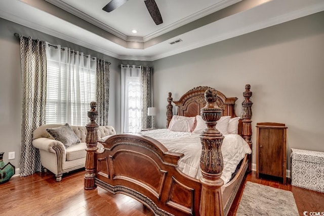 bedroom featuring wood finished floors, visible vents, ceiling fan, ornamental molding, and a raised ceiling