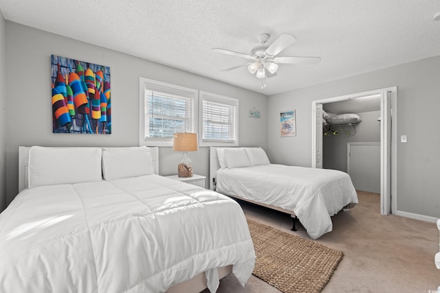 bedroom featuring light carpet, a textured ceiling, ceiling fan, a closet, and a walk in closet