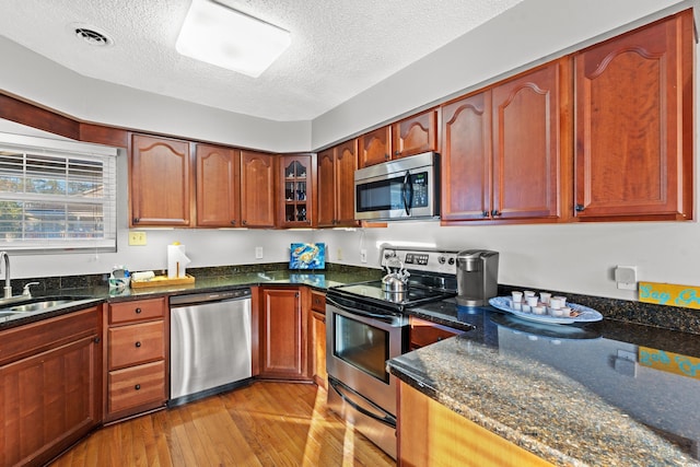 kitchen featuring stainless steel appliances, light hardwood / wood-style floors, sink, dark stone countertops, and a textured ceiling