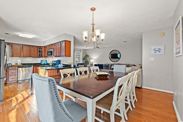 dining room with ceiling fan with notable chandelier, light hardwood / wood-style flooring, and a textured ceiling