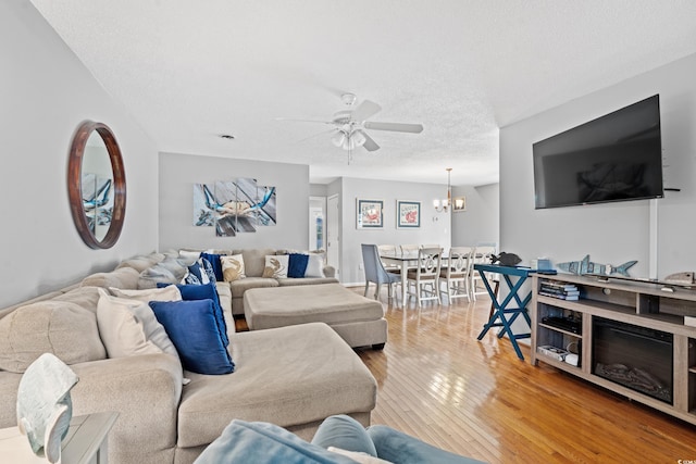 living room with hardwood / wood-style flooring, ceiling fan with notable chandelier, and a textured ceiling