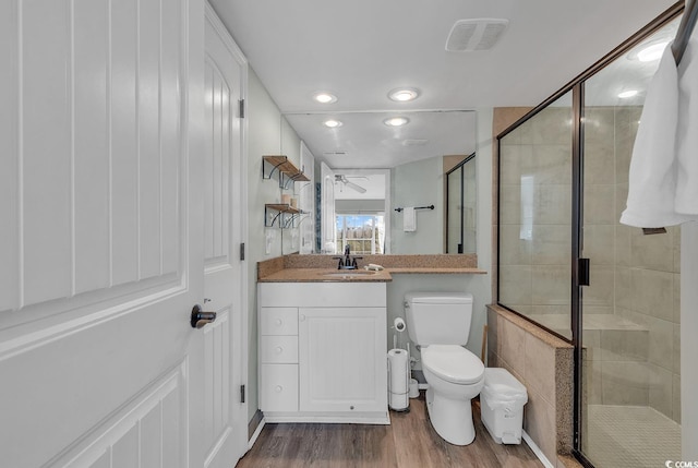 bathroom with a shower with shower door, hardwood / wood-style floors, toilet, ceiling fan, and vanity