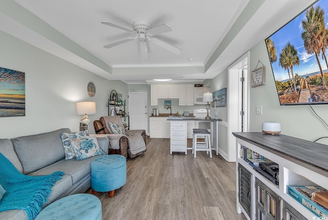 living room with a raised ceiling, wood finished floors, a ceiling fan, and crown molding