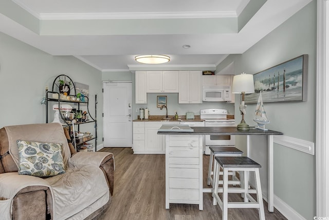 kitchen with white appliances, wood finished floors, white cabinetry, a breakfast bar, and crown molding
