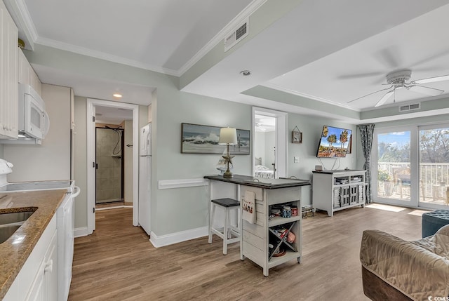 kitchen with white appliances, ceiling fan, light wood finished floors, white cabinetry, and a raised ceiling