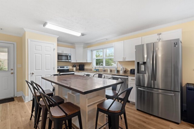 kitchen featuring stainless steel appliances, white cabinetry, light hardwood / wood-style flooring, and ornamental molding