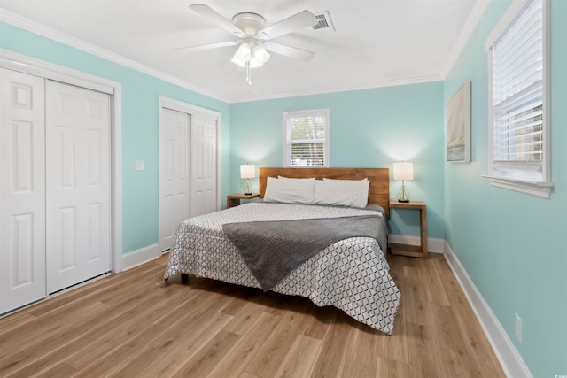 bedroom featuring ornamental molding, multiple closets, light hardwood / wood-style flooring, and ceiling fan