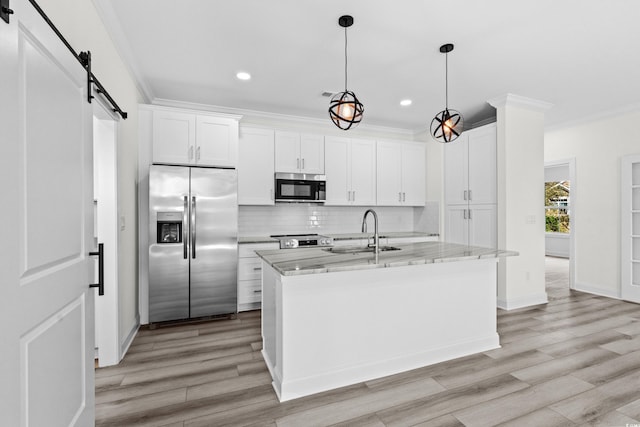 kitchen featuring white cabinets, a barn door, a center island with sink, stainless steel appliances, and sink