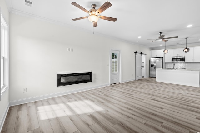 unfurnished living room featuring ornamental molding, light wood-type flooring, and a barn door