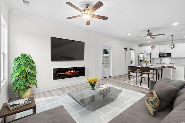 living room with ornamental molding, ceiling fan, light wood-type flooring, and a barn door