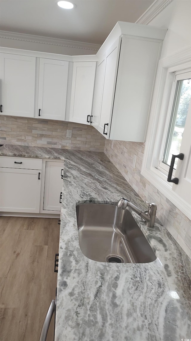 kitchen with a sink, light stone counters, backsplash, and white cabinets