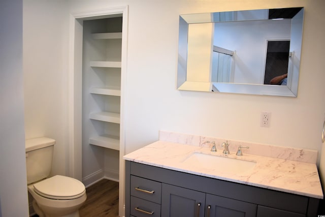 bathroom featuring vanity, built in shelves, wood finished floors, baseboards, and toilet