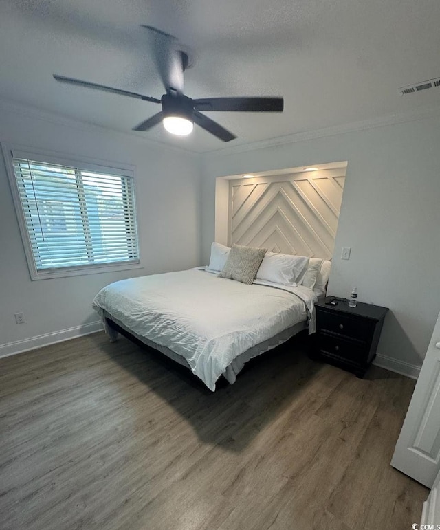 bedroom featuring visible vents, baseboards, wood finished floors, and crown molding