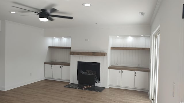 unfurnished living room featuring a ceiling fan, wood finished floors, visible vents, a fireplace with raised hearth, and crown molding