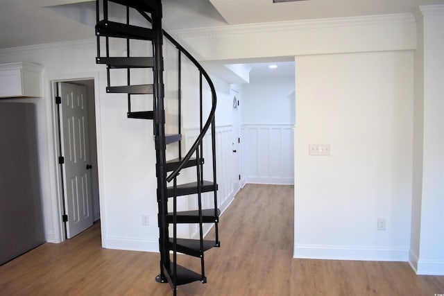 stairway with wainscoting, baseboards, wood finished floors, and crown molding