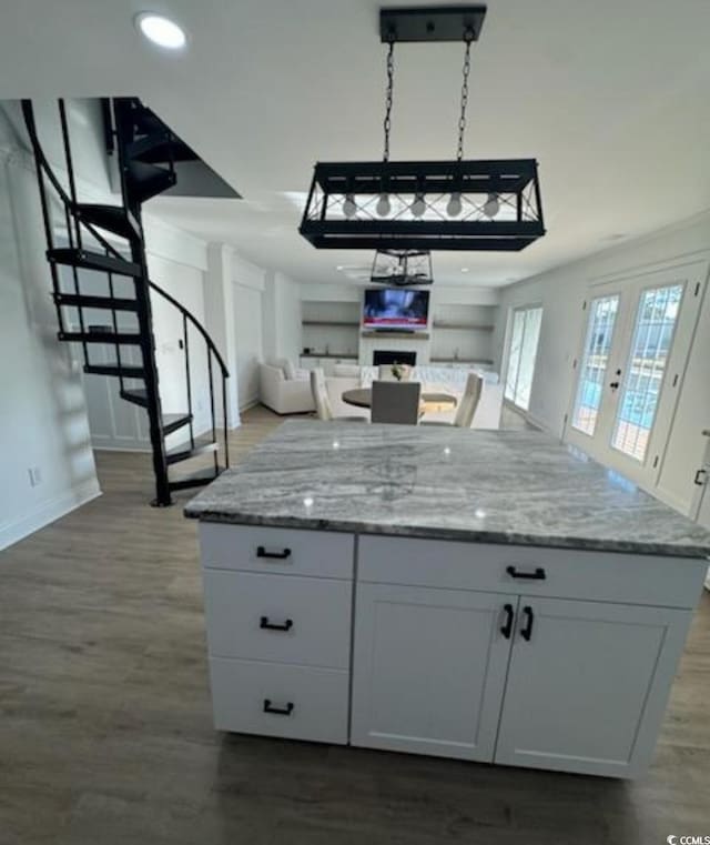 kitchen featuring dark wood-type flooring, light stone counters, a kitchen island, open floor plan, and white cabinets