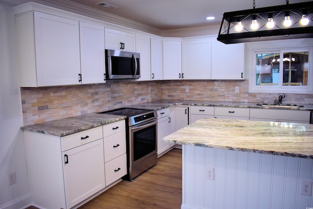 kitchen featuring light stone counters, wood finished floors, appliances with stainless steel finishes, white cabinets, and decorative backsplash