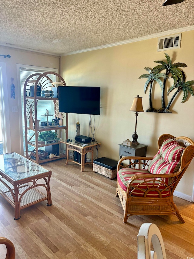 sitting room with light hardwood / wood-style floors, a textured ceiling, and ornamental molding