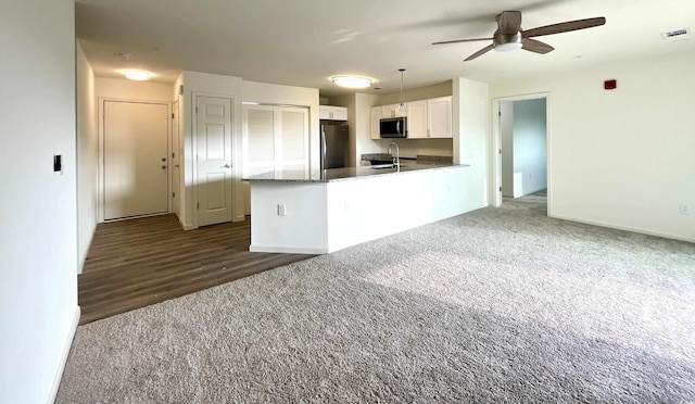 kitchen with stainless steel appliances, a sink, white cabinets, dark colored carpet, and ceiling fan