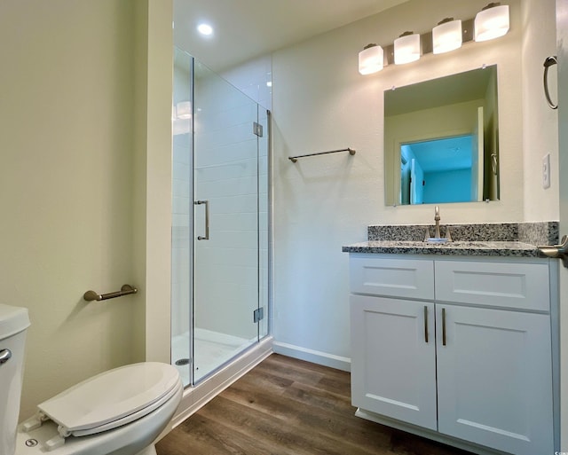 bathroom featuring toilet, vanity, wood-type flooring, and a shower with door