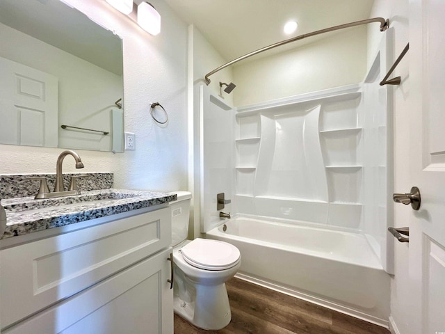 bathroom with wood finished floors,  shower combination, toilet, vanity, and a textured wall