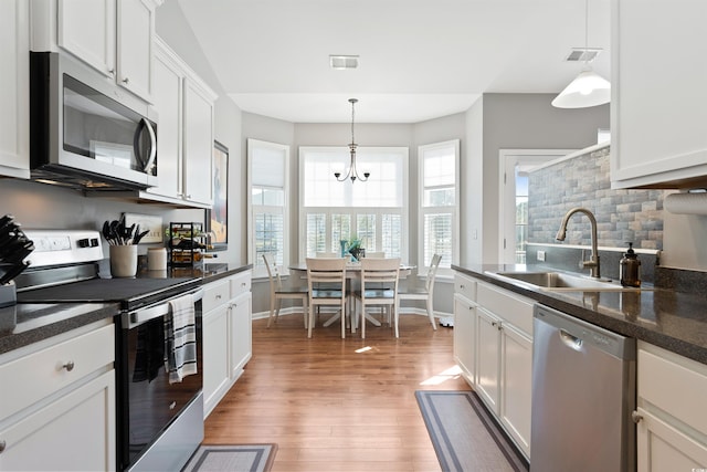 kitchen featuring appliances with stainless steel finishes, wood-type flooring, sink, hanging light fixtures, and white cabinetry