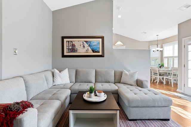 living room with an inviting chandelier, wood-type flooring, and vaulted ceiling