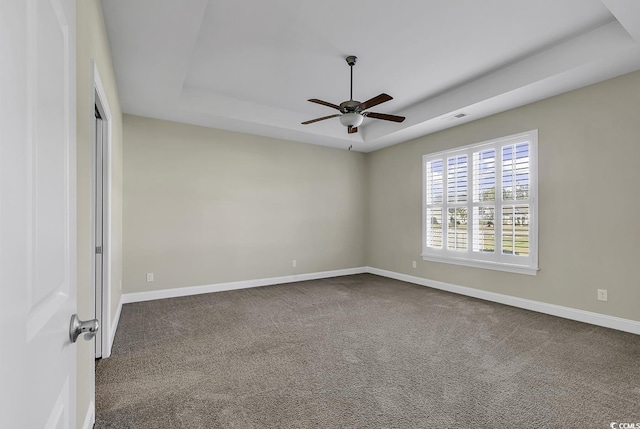 unfurnished room with a raised ceiling, a ceiling fan, dark carpet, and baseboards