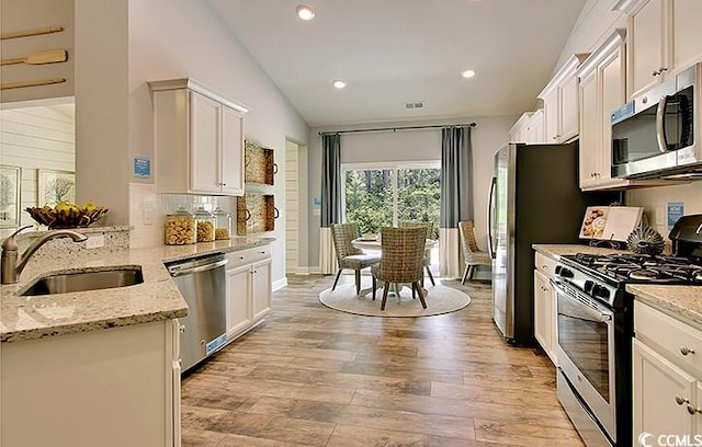 kitchen featuring stainless steel appliances, light stone countertops, vaulted ceiling, light wood-type flooring, and white cabinetry