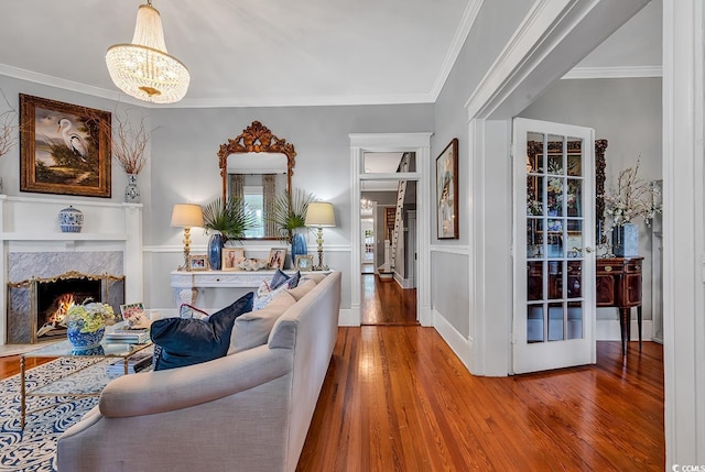 living room with an inviting chandelier, crown molding, a high end fireplace, and hardwood / wood-style flooring