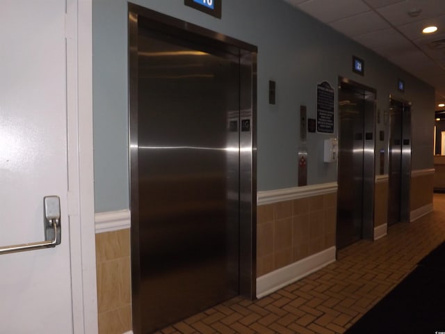 corridor featuring elevator and tile walls