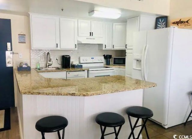 kitchen featuring white cabinetry, a breakfast bar area, white appliances, and kitchen peninsula